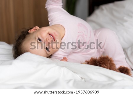 Authentic portrait caucasian little infant chubby baby girl or boy in pink sleepy upon waking looking at camera smiling cute and grimaces in white bed. Child care, Childhood, Parenthood, life concept