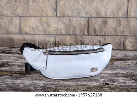 White men's women's bag. Sporty style. A small bag with handles on the lock. The background is white brick. Waist bag, hung on the belt.