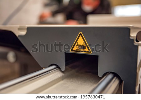 A warning sign on a woodworking machine. Production safety in a carpentry workshop. Hazard sign of moving parts in yellow triangle with hands