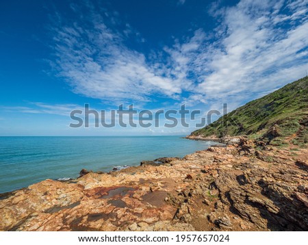 Picture of a cliff on the sea with blue water. Green trees