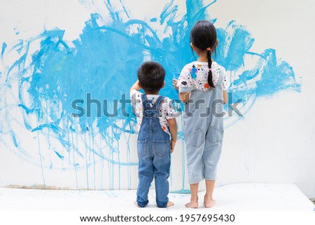 Unidentified sibling helping together to paint the wall with water color with happiness moment, concept of art education for kid, homeschooling and learn through play activity for child development.