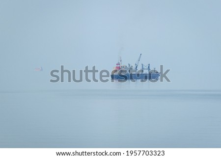 Cargo ship anchored in the sea on a foggy morning.  The sea merges with the horizon.  Batumi, Georgia. Photo with soft focus.