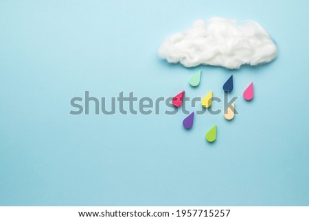 Multicolored drops fall from a cloud on a blue background. Collage of modern art. Climate picture.