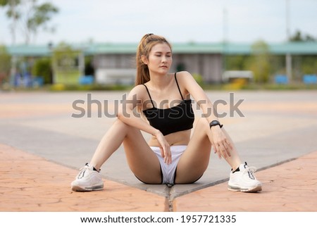 The running girl sit-down on ground for relax muscle after she jogging in morning , she acting and post for take photo relax on time