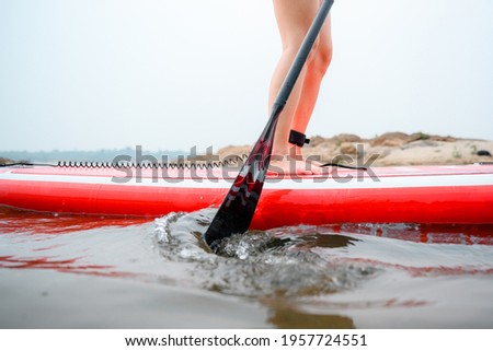 Stand up paddleboarding women paddle on the beach Happily on a paddleboard on the red water. Close up picture Young model legs on the beach during the summer vacation