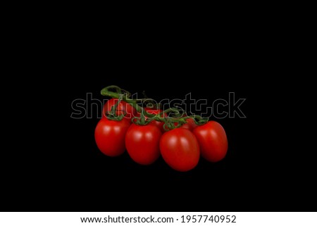 Seven ripe cherry tomatoes on branches, on a black background. 