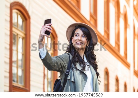 Tourist posing for a selfie in a street. Vlogger recording content for her travel vlog. Cute young smiling girl is making selfie on a camera while walking outdoors.