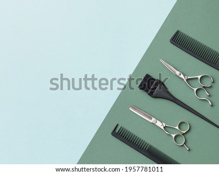 Hairdressing tools on a green background and a blue sheet with space for text. Black and steel hair salon accessories, comb and scissors.