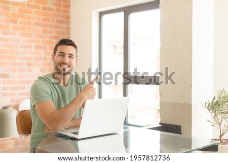 handsome man smiling cheerfully, feeling happy and pointing to the side and upwards, showing object in copy space