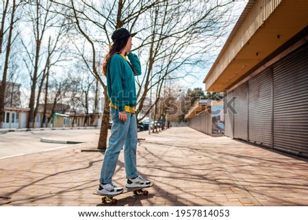 A young Caucasian hipster woman rides down the street on a skateboard. In the background, an alley. Copy space. Concept of sports lifestyle and street culture.