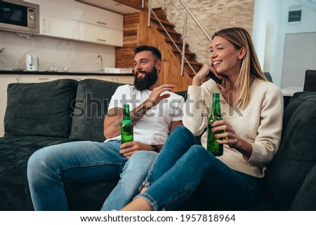 Young beautiful couple relaxing at home on the sofa while drinking beer and watching television together