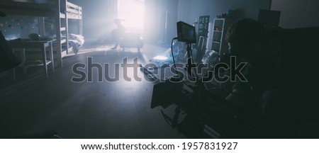 Director of photography with a camera in his hands on the set. Professional videographer at work on filming a movie, commercial or TV series. Filming process indoors, studio Royalty-Free Stock Photo #1957831927
