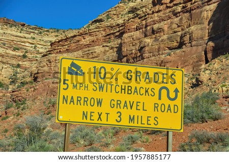 Low angle close up of a yellow road warning sign for truck warning of switchbacks, gravel and steep grades, with red rocks of West Coast, United States of America mountains in background