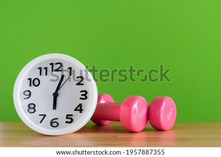 Time for exercising clock and dumbbell on the table with green background