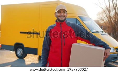 Indian man delivering package. Holding cardboard box in front of the van. High quality photo