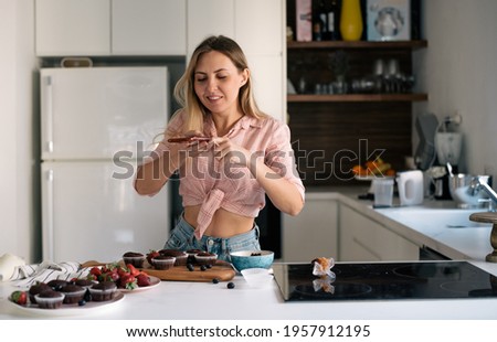 Girl cook cupcake and make photo of food. caucasian concentrated woman wearing t-shirt taking photo muffins on cellphone in modern kitchen.