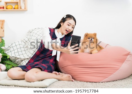 Young woman using Mobile phone selfie with a small dog in the living room. Pomeranian in living room with a girl.