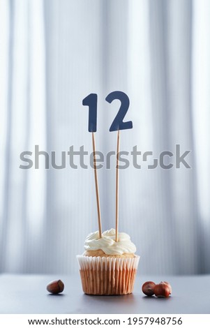 Fresh tasty homemade creamy cupcake or muffin with creamy topping and number 12 twelve and bright background. Birthday greeting card concept. High quality vertical image