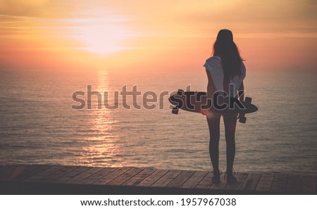 Beautiful girl with a skateboard looking to the sunset