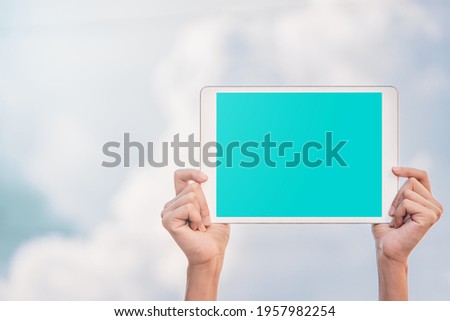 Technology advertisement concept: Two hands holding mock-up white tablet which has a blue blank clipping path screen outdoor with a cloudy sky background.