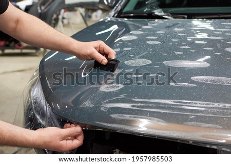 Installation of a protective paint and varnish transparent film on the car. PPF polyurethane film to protect the car paint from stones and scratches. Royalty-Free Stock Photo #1957985503