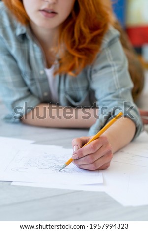 Drawing hobby. Art school. Creative skill talent. Left-handed red-haired female artist sketching with pencil in hand on white paper on light blur background.