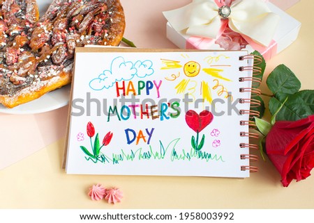 Happy Mother day still life. Breakfast for mum sweet pizza, red rose, gift and hand drawing in the album made by the child for mom. Text card Happy Mothers day.