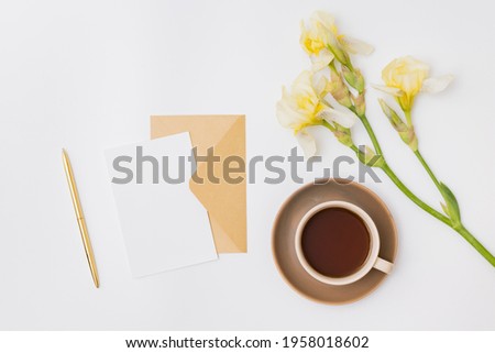 Mockup white greeting card and envelope with yellow irises, cup with coffee on a white background