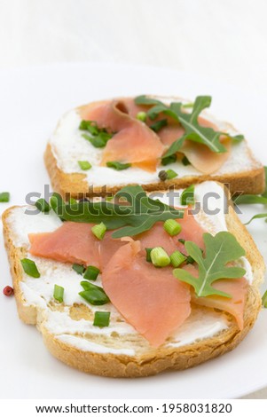 Toast with chum salmon fish, cottage cheese, green onions and arugula on wheat bread on a white plate