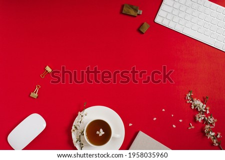 The workplace of a female blogger with a computer keyboard, office, apple tree flowers, tea in a cup on a red background. Flat lay, top view, copy space. Spring and Valentine's Day Concept