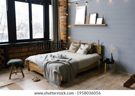 Double bed with natural natural accents on the sheets and beige pillows in the grey Scandinavian bedroom, copy space on the paintings on the shelf above the bed Royalty-Free Stock Photo #1958036056