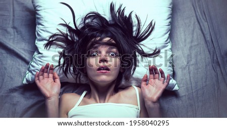 Young girl with a frightened expression wakes up from a nightmare in bed. Woman had a terrible unpleasant dream, she is experiencing a panic attack. Life stress, mental health problems and insomnia. Royalty-Free Stock Photo #1958040295