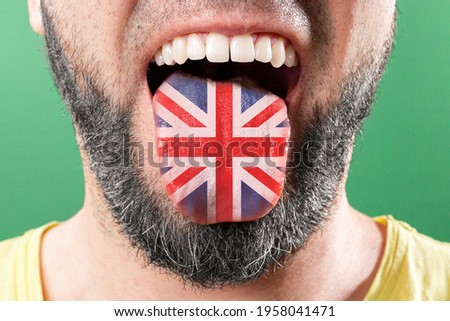 Native speaker. The protruding tongue of a bearded man is close-up, in the colors of the English flag. The concept of learning foreign languages.