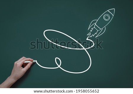 hand draws in chalk on a blackboard a rocket flying upward, the concept of a quick start, success, big profit and stock market value