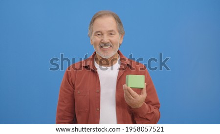 Satisfied man with green box in hand in front of a blue background. Creative people can put the product they want into the man's hand. 