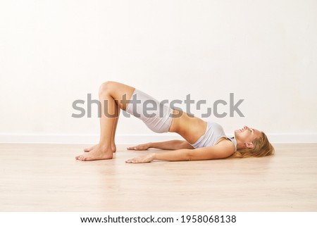 Young pretty woman standing in pelvic brigde. Yoga exercise at gym. Home sport workout. Elbows static balance stand. Floor stretching. Healthy lifestyle. Long blond hair. Smiling female person. Side Royalty-Free Stock Photo #1958068138
