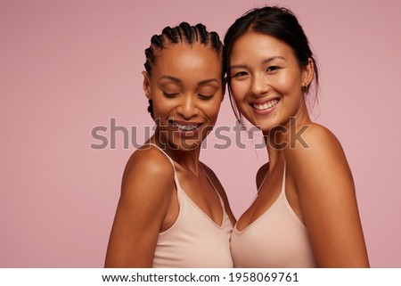 Two attractive mixed race women on pink background. Women with natural beauty smiling while standing close to each other. Royalty-Free Stock Photo #1958069761