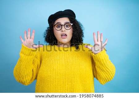 Young beautiful woman wearing french look with beret and yellow casual sweater over isolated blue background showing and pointing up with fingers number ten while smiling confident and happy