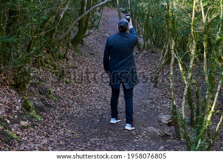 Man in coat and mask, photographing the forest with a mobile