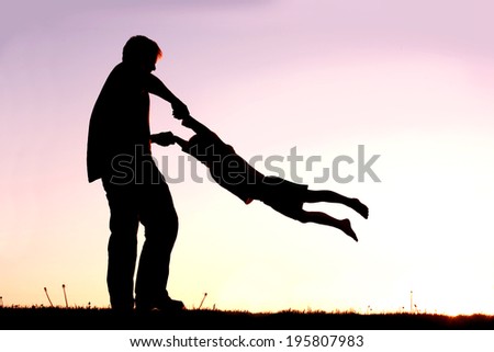 A silhouette of a playful young father spinning and dancing with his little child outside at sunset on a summer day. Royalty-Free Stock Photo #195807983
