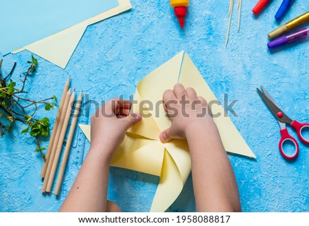 Step-by-step making of a paper weather vane by a child on a blue concrete background. Children's creativity, divas, crafts. Paper crafts Royalty-Free Stock Photo #1958088817