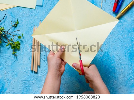 Step-by-step making of a paper weather vane by a child on a blue concrete background. Children's creativity, divas, crafts. Paper crafts Royalty-Free Stock Photo #1958088820