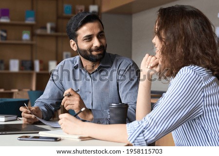 Interview of happy smiling indian hr manager with latin young professional and friendly support discussing job cv. Mentoring Hispanic male teacher and female student in multiethnic creative space. Royalty-Free Stock Photo #1958115703