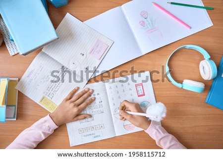 Table top closeup view of kid student hands writing doing math homework exercises in notebook with book on table. Learning classes for elementary school pupils. Study at home classroom concept. Royalty-Free Stock Photo #1958115712