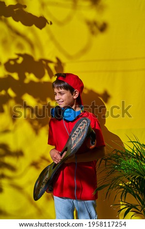 Vertical photo Portrait of a boy with headphones and a skateboard on yellow background and shadows of trees