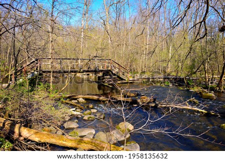 Beautiful wooden bridge goes over the Oconomowoc River along the Monches Ice Age Trail near Merton Wisconsin on a beautiful spring April afternoon.  The small section of river is surrounded by forest. Royalty-Free Stock Photo #1958135632