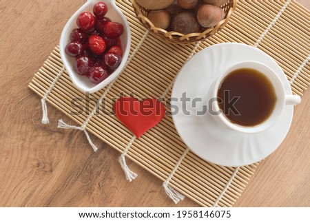 Composition from a cup of coffee, a nut in a basket, berries and a red heart. Angle of view, top.