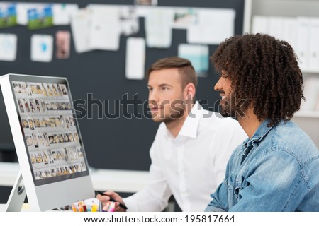 Creative team editing a photo shoot with a young trendy African American man and a male coworker working on a computer monitor together