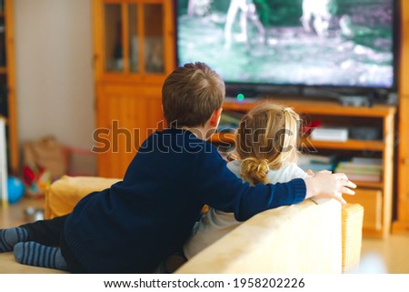 Cute little toddler girl and school kid boy watching animal movie or movie on tv. Happy healthy children, siblings during coronavirus quarantine staying at home. Brother and sister together. no face