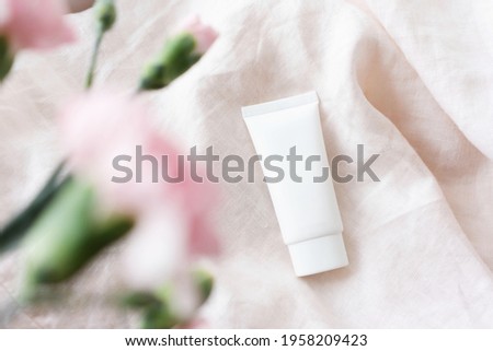 white cosmetic tube with face cream, body lotion or cleanser  on a light fabric background with pink flowers. Sensitive skin care concept. Copy space, mock up Royalty-Free Stock Photo #1958209423